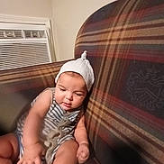 Devon joined the competition — help win amazing prizes! air_conditioner, baby, child, couch, cozy, curious, cute, focused, home, indoor, infant, knit_hat, person, plaid_couch, sitting, soft_lighting, striped_clothing, toy, white_hat, young_child
