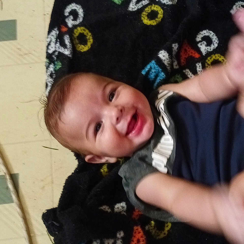 Devon joined the competition — help win amazing prizes! baby, blanket, casual, child, clothing, colorful, cute, expression, face, floor, happy, indoor, infant, lying_down, person, playful, portrait, smiling, tiled_floor, young_child