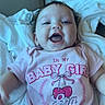 baby, bed, bedroom, blanket, child, cozy, eyes, face, girl, happy, indoor, infant, laughing, lying_down, mouth, onesie, pink_clothing, portrait, smiling, text_on_clothing