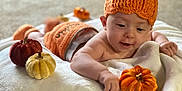 Miami is registered to the contest to win money with this photo: baby, infant, pumpkin_hat, pumpkin_outfit, plush_pumpkin, blanket, autumn, fall, decorations, soft_texture, indoors, cute, child, smiling, orange, red, yellow, happy, cozy, playful