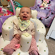 Miami is registered to the contest to win money with this photo: baby, infant, smiling, sitting, inflatable_chair, bib, pink_pants, pacifier, toy, minnie_mouse_chair, carpet, indoor, happy, child, cute, person, furniture, room, play_area, colorful