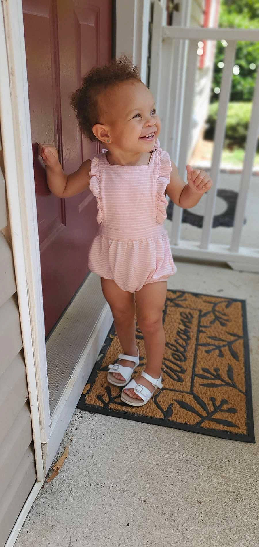 Zaria is registered to the contest to win money with this photo: baby, baby_toddler_clothing, cheek, child, face, flooring, gesture, happy, head, human_leg, knee, leg, person, pink, sleeve, smile, sock, thigh, toddler, waist