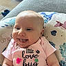 baby, baby_bed, child, cushion, cute, dinosaur_pattern, face, happy, head, home, indoor, infant, onesie, person, pink_clothing, portrait, skin, smiling, toddler, tongue_out