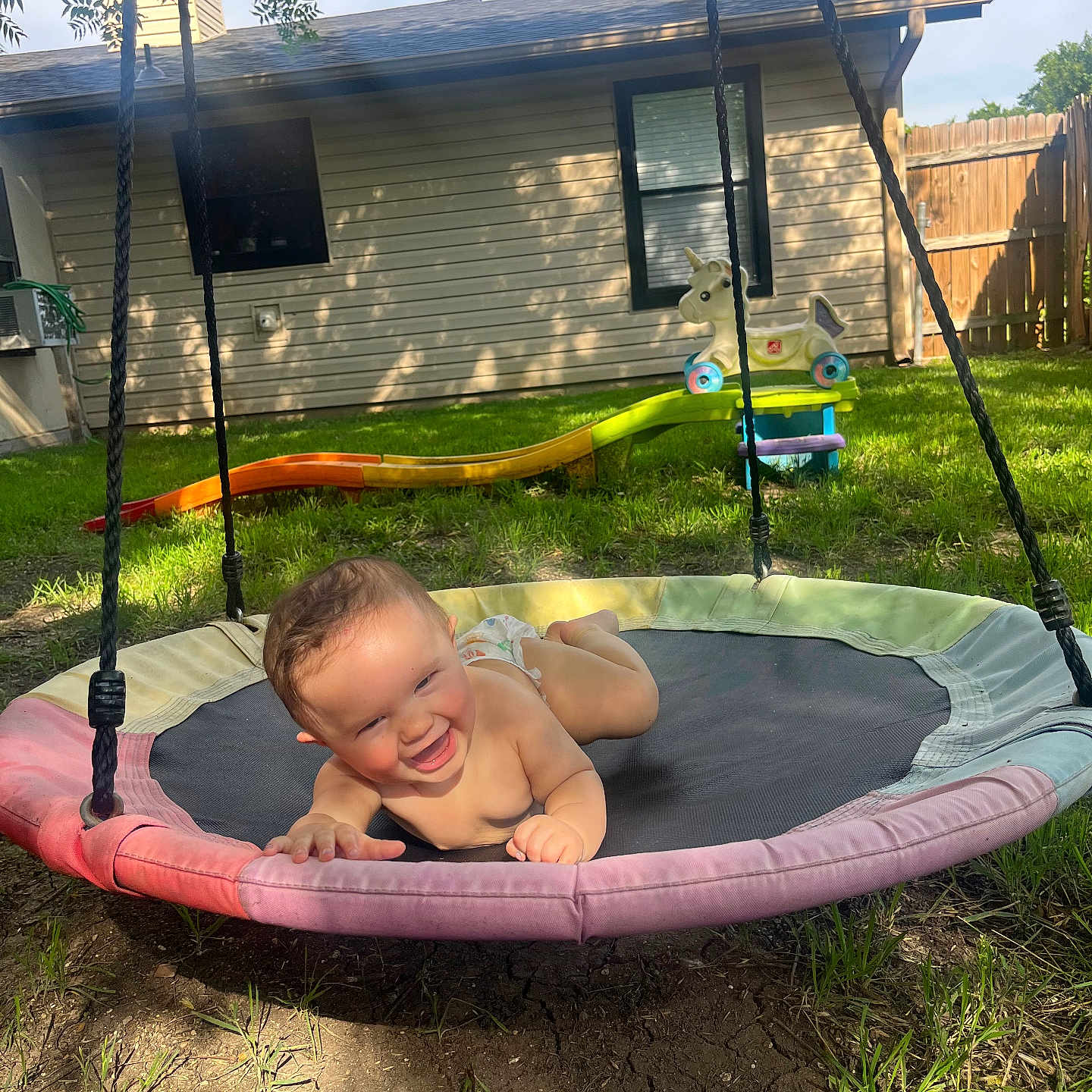 Arya is registered to the contest to win money with this photo: baby, backyard, child, grass, happy, house, infant, nature, outdoor, plastic_toy, play, playground, rope, shade, slide, smile, sunlight, swing, toy, unicorn