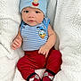 Joab is registered to the contest to win money with this photo: baby, infant, child, blue_hat, teddy_bear_patch, striped_shirt, donald_duck, red_pants, patterned_socks, blanket, cozy, cute, portrait, indoors, soft_texture, smiling, small_hands, seated, comfortable, warm