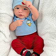 Joab is registered to the contest to win money with this photo: baby, infant, child, blue_hat, teddy_bear_patch, striped_shirt, donald_duck, red_pants, patterned_socks, blanket, soft_texture, cozy, cute, portrait, indoor, smiling_face, raising_fist, young_child, comfortable, warm