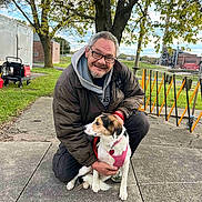 Angel joined the competition — help win amazing prizes! man, dog, outdoor, tree, sidewalk, grass, jacket, glasses, smile, leash, harness, autumn, urban, building, fence, casual_clothing, pet, kneeling, daytime, nature
