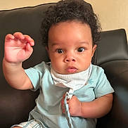Karson is registered to the contest to win money with this photo: baby, child, curly_hair, light_blue_shirt, pacifier_clip, sitting, leather_chair, indoors, cute, portrait, young_child, face, hand, expression, eyes, clothing, furniture, background, skin, infant