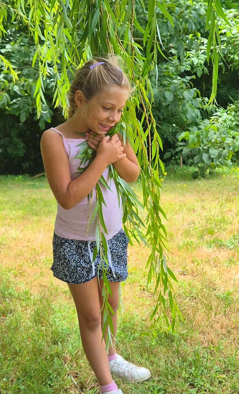 Liah a rejoint le concours — aidez-le/la à gagner de superbes lots ! barefoot, casual_clothing, child, daylight, girl, grass, greenery, happy, leaves, nature, outdoor, playful, portrait, shorts, smiling, summer, tank_top, tree, white_shoes, willow_branch