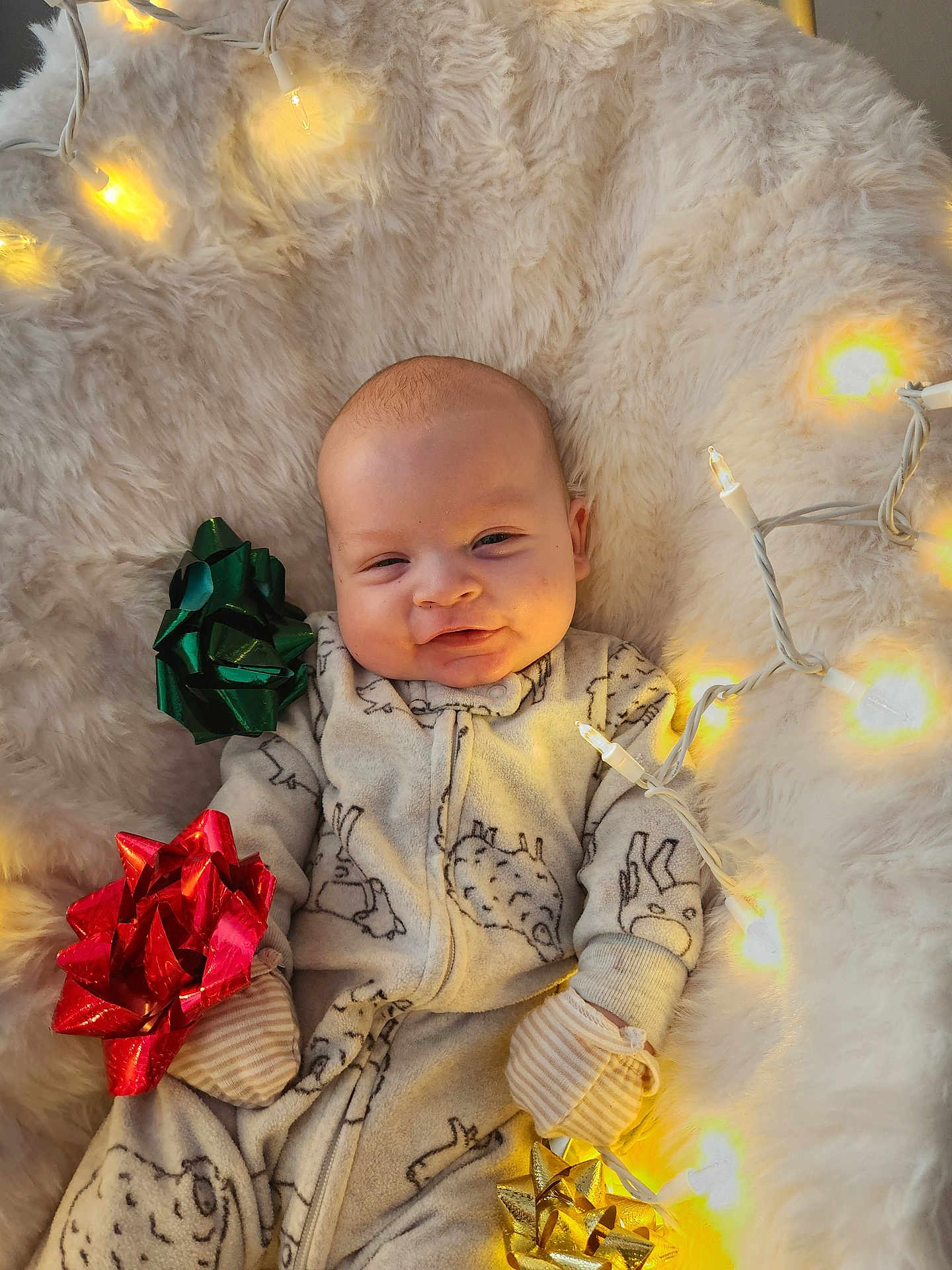 Jasper joined the competition — help win amazing prizes! baby, infant, onesie, animal_print, mittens, fluffy_rug, fairy_lights, glowing_lights, gift_bows, red_bow, green_bow, gold_bow, smile, face, cute, holiday_theme, cozy, indoor, portrait, soft_texture