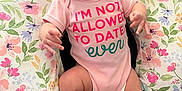 Esmé joined the competition — help win amazing prizes! baby, infant, pout, headband, pink, onesie, text_on_clothing, floral_pattern, cushion, seated, indoor, expression, cute, child, person, leg, arm, face, skin, fabric