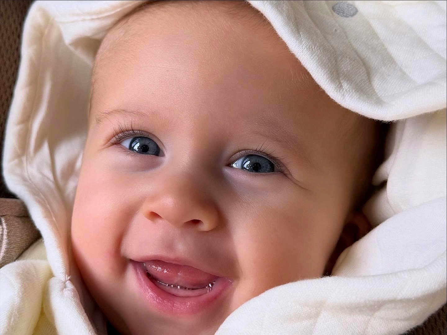 Ava is registered to the contest to win money with this photo: baby, smiling, close_up, face, blue_eyes, blanket, hood, infant, cute, happy, skin, portrait, child, young, adorable, expression, teeth, soft_texture, warm, cozy