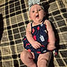 baby, child, infant, headband, bow, plaid, blanket, dress, lying_down, expression, surprised, skin, legs, arms, indoors, cute, person, young, smiling, happy