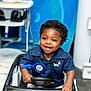 child, toddler, smiling, toy_car, blue_shirt, ribbon, indoor, happy, face, hands, steering_wheel, short_hair, cute, play, person, seat, clothing, background, baby, portrait