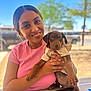 brown_puppy, cute, dog, eyes, fence, holding_pet, jewelry, outdoor, person, pink_tshirt, portrait, puppy, ring_jewelry, shallow_depth_of_field, short_hair, smiling, sunny, table, tattoo, tree