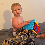 Malachi is registered to the contest to win money with this photo: bed, blanket, child, colorful, comfort, curious, diaper, expression, face, furniture, indoor, person, plush, room, shadow, sitting, skin, toddler, toy, young_child
