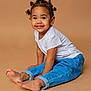 Nïna a rejoint le concours — aidez-le/la à gagner de superbes lots ! child, toddler, smile, portrait, studio, jeans, white_tshirt, bare_feet, sitting, cute, brown_background, hair_buns, pigtails, earrings, happy, playful, young_child, pose, photography, eyes