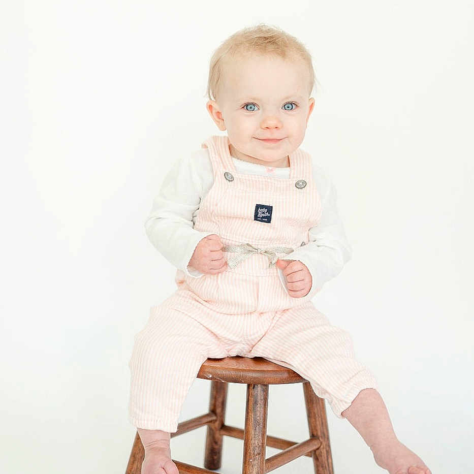 Kenzy is registered to the contest to win money with this photo: baby, barstool, bodypart, chair, clothing, face, finger, footwear, furniture, hand, head, longsleeve, pants, person, photography, portrait, shoe, sitting, sleeve, wood