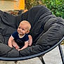baby, child, blue_eyes, smiling, sitting, black_chair, outdoor, greenery, cushion, cute, infant, happy, person, portrait, blond_hair, casual_clothing, floor, daylight, nature, relaxing