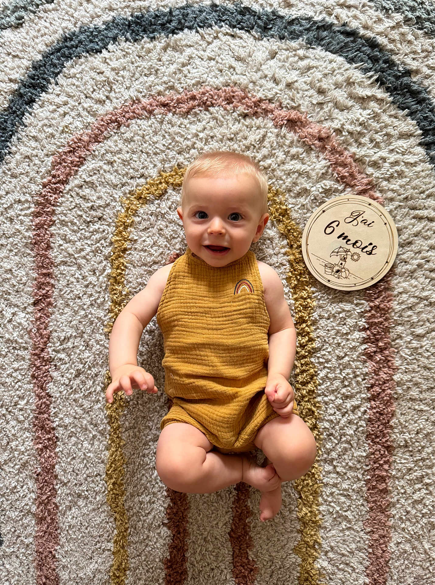 émile participe au concours pour gagner de l'argent avec cette photo : baby, infant, child, smiling, romper, mustard_color, milestone, plaque, rug, textured_rug, concentric_circles, floor, indoor, person, cute, happy, six_months, milestone_marker, portrait, lying_down