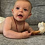 émile participe au concours pour gagner de l'argent avec cette photo : baby, child, infant, face, eyes, mouth, arm, hand, necklace, toy, plush_toy, wooden_ring, couch, gray_couch, fabric, skin, expression, curious, lying_down, indoors