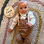 baby, brown_clothing, carpet, child, cute, eyes, face, floor, hand, indoors, infant, milestone, overalls, person, portrait, rug, text, toddler, white_socks, wooden_sign