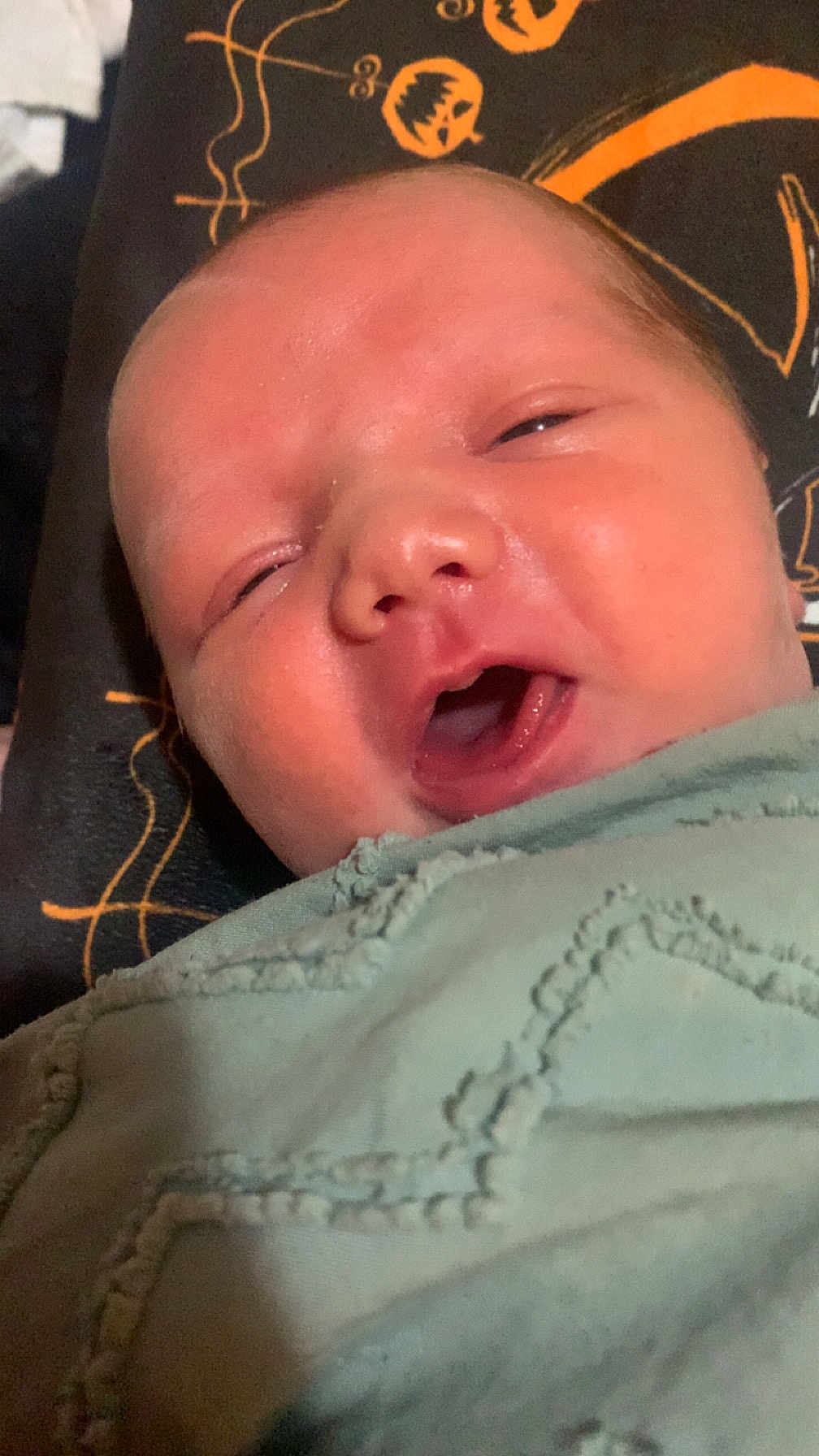 Easton joined the competition — help win amazing prizes! baby, newborn, face, closeup, blanket, sleepy, mouth_open, skin, infant, person, child, soft, texture, clothing, pattern, orange, dark_background, lying_down, cute, portrait