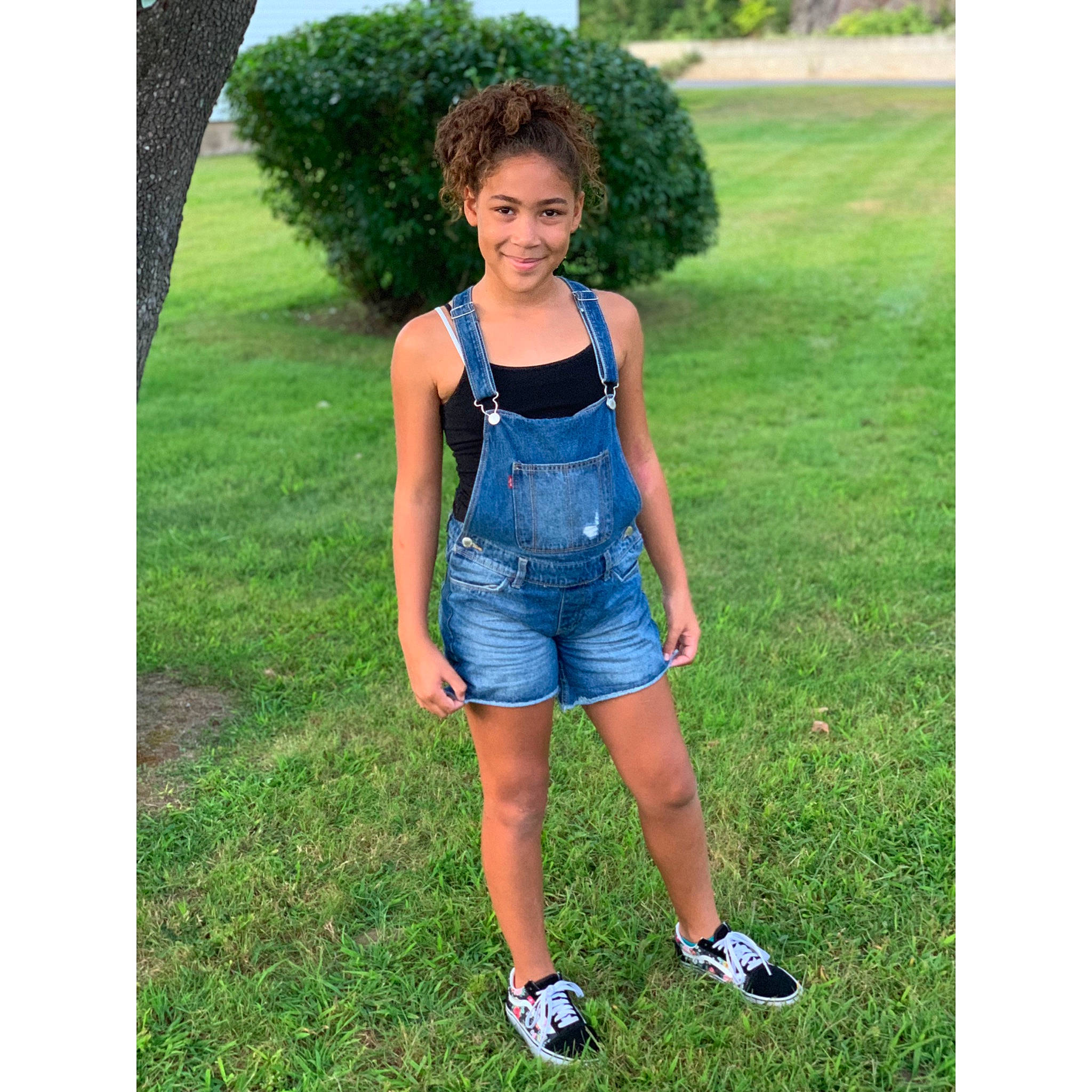 Tianna is registered to the contest to win money with this photo: blue, child, clothing, crop_top, denim, dress, electric_blue, footwear, grass, jean_short, jeans, joy, overall, person, pocket, shoe, shorts, summer, t_shirt, textile