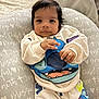 baby, infant, child, cute, face, clothing, sweatshirt, pants, cushion, text, pattern, indoor, portrait, looking, hands, soft, comfortable, young, smiling, cozy