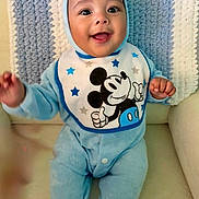 Teodoro is registered to the contest to win money with this photo: baby, child, smiling, blue_onesie, mickey_mouse, bib, knitted_blanket, chair, happy, infant, portrait, seated, cute, indoors, cozy, face, hands, clothing, babywear, soft_texture
