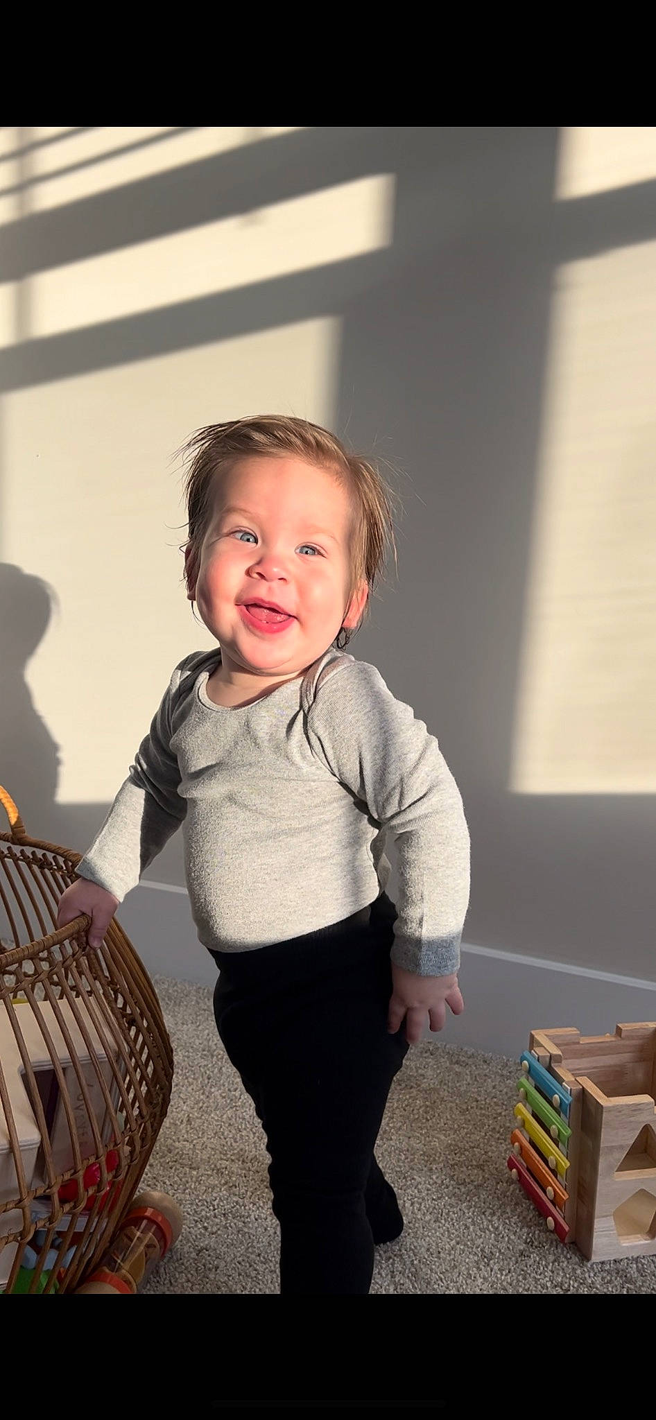 Riley is registered to the contest to win money with this photo: baby_toddler_clothing, box, child, face, flash_photography, flooring, folk_instrument, fun, happy, pattern, person, play, room, sitting, sleeve, smile, standing, sweatpant, t_shirt, toddler