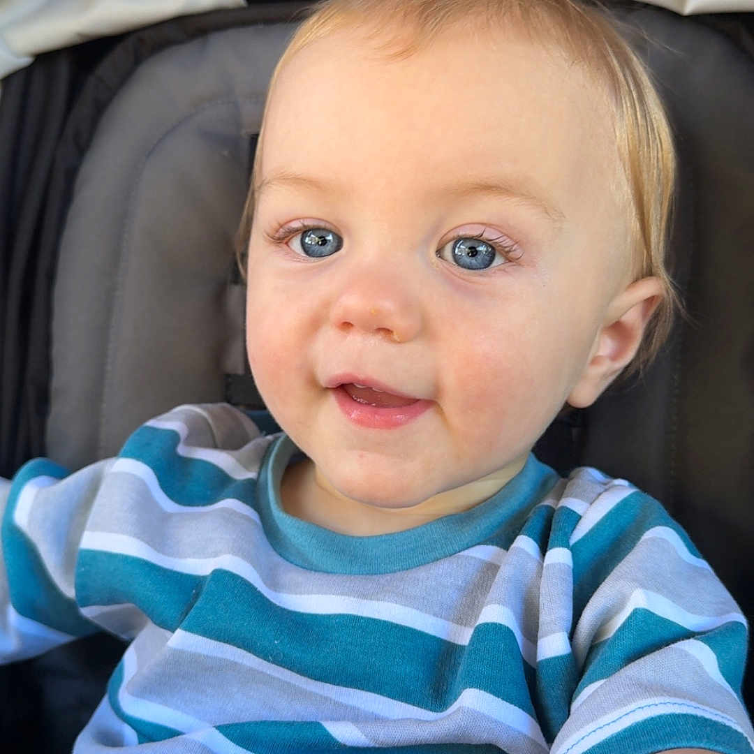 Titan is registered to the contest to win money with this photo: toddler, child, baby, blue_eyes, striped_shirt, sitting, stroller, blanket, curious, portrait, indoor, clothing, person, face, head, cute, happy, skin, hair, expression