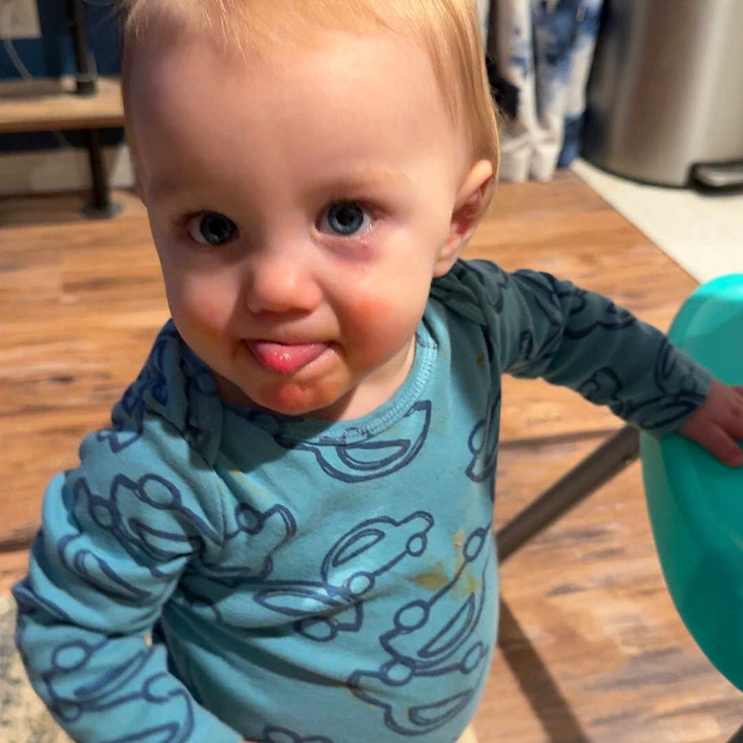 Titan is registered to the contest to win money with this photo: baby, blue_clothing, car_pattern, child, curtains, cute, expression, furniture, hair, home, indoor, pajamas, person, playful, rug, standing, toddler, tongue_out, walker, wooden_floor