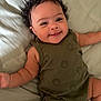 Eliza is registered to the contest to win money with this photo: baby, infant, smiling, curly_hair, green_outfit, smiley_faces, lying_down, bed, soft_bedding, cute, happy, child, skin, face, arm, legs, one_person, indoors, casual_clothing, portrait