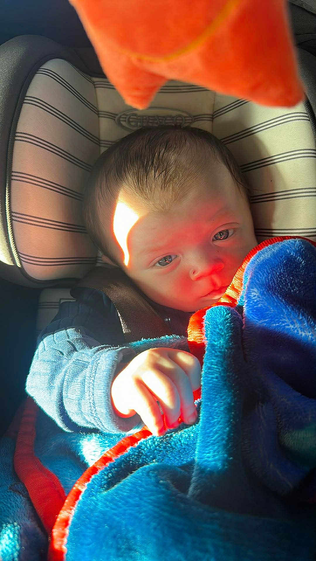 Logan joined the competition — help win amazing prizes! baby, infant, child, car_seat, blanket, plush_toy, sunlight, portrait, hand, seatbelt, buckle, stripes, blue_blanket, cozy, sleepy, closeup, car_interior, expression, soft_texture, fabric