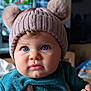 baby, child, blue_eyes, knit_hat, pom_poms, cute, portrait, indoor, hand, rings, clothing, teal_outfit, face, expression, closeup, soft_lighting, cozy, adorable, curious, infant