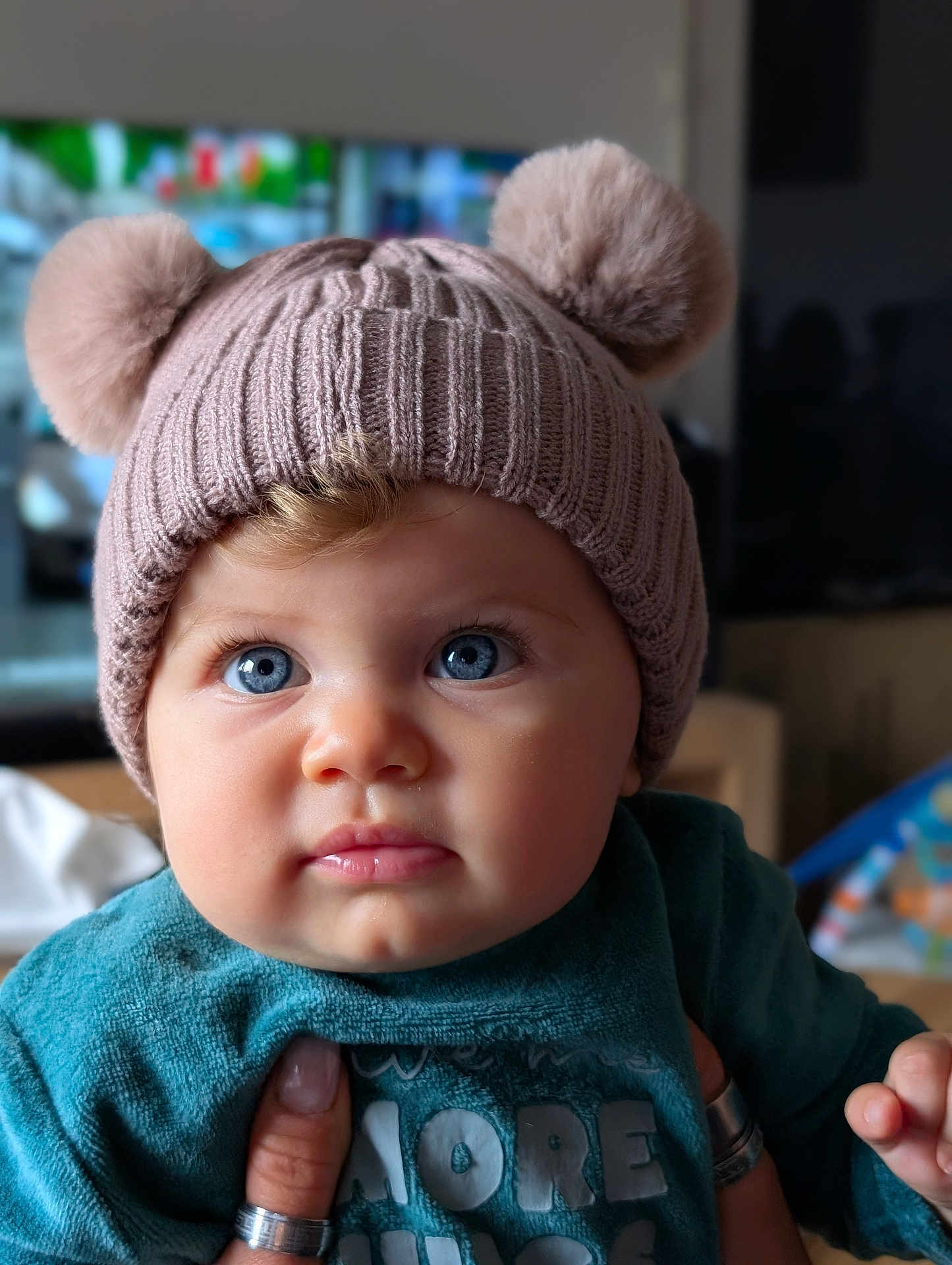 Lily-Rose a rejoint le concours — aidez-le/la à gagner de superbes lots ! baby, child, blue_eyes, knit_hat, pom_poms, cute, portrait, indoor, hand, rings, clothing, teal_outfit, face, expression, closeup, soft_lighting, cozy, adorable, curious, infant