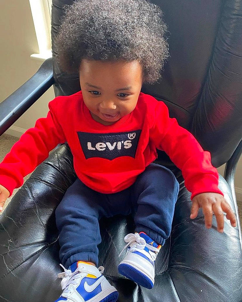 Maurice is registered to the contest to win money with this photo: afro, arm, baby_toddler_clothing, black, blue, cap, car_seat, clothing, comfort, cool, facial_expression, finger, hairstyle, happy, leg, organ, outerwear, person, sleeve, toddler