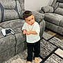 Liam is registered to the contest to win money with this photo: toddler, child, couch, controller, gaming_controller, living_room, carpet, recliner, white_sweater, black_pants, tan_shoes, gold_chain, floor, furniture, indoors, person, young_child, standing, home, casual_clothing