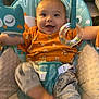baby, smiling, happy, infant, toy, seat, clothing, orange_shirt, patterned_pants, indoor, child, face, person, playful, comfort, cushion, hand, foot, bright, cute