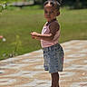 Naëlys participe au concours pour gagner de l'argent avec cette photo : toddler, child, girl, outdoor, standing, denim_shorts, pink_tank_top, hair_puff, serious_expression, sunlight, patterned_floor, grass, nature, summer, footwear, sandals, portrait, person, daylight, casual_clothing