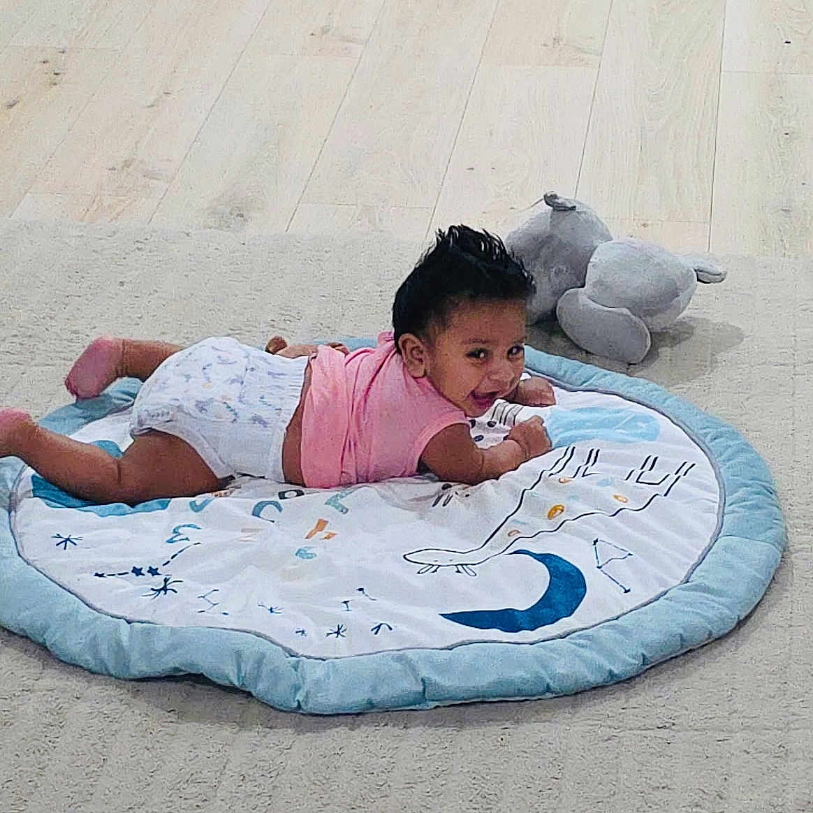 Ricky joined the competition — help win amazing prizes! baby, child, diaper, pink_shirt, play_mat, smiling, toy, plush_elephant, floor, wooden_floor, indoor, cute, lying_down, happy, infant, person, toddler, carpet, home, playtime