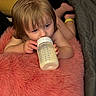 toddler, baby, bottle, milk, pink_cushion, blonde_hair, child, indoors, blanket, cozy, soft_texture, lying_down, feeding, cute, young_child, person, skin, hand, foot, relaxing