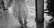 Heavenly is registered to the contest to win money with this photo: toddler, child, barefoot, dress, wet_floor, porch, black_and_white, outdoor, back_view, post, rope, grass, concrete, small_person, young_child, single_child, nature, daylight, curly_hair, walking
