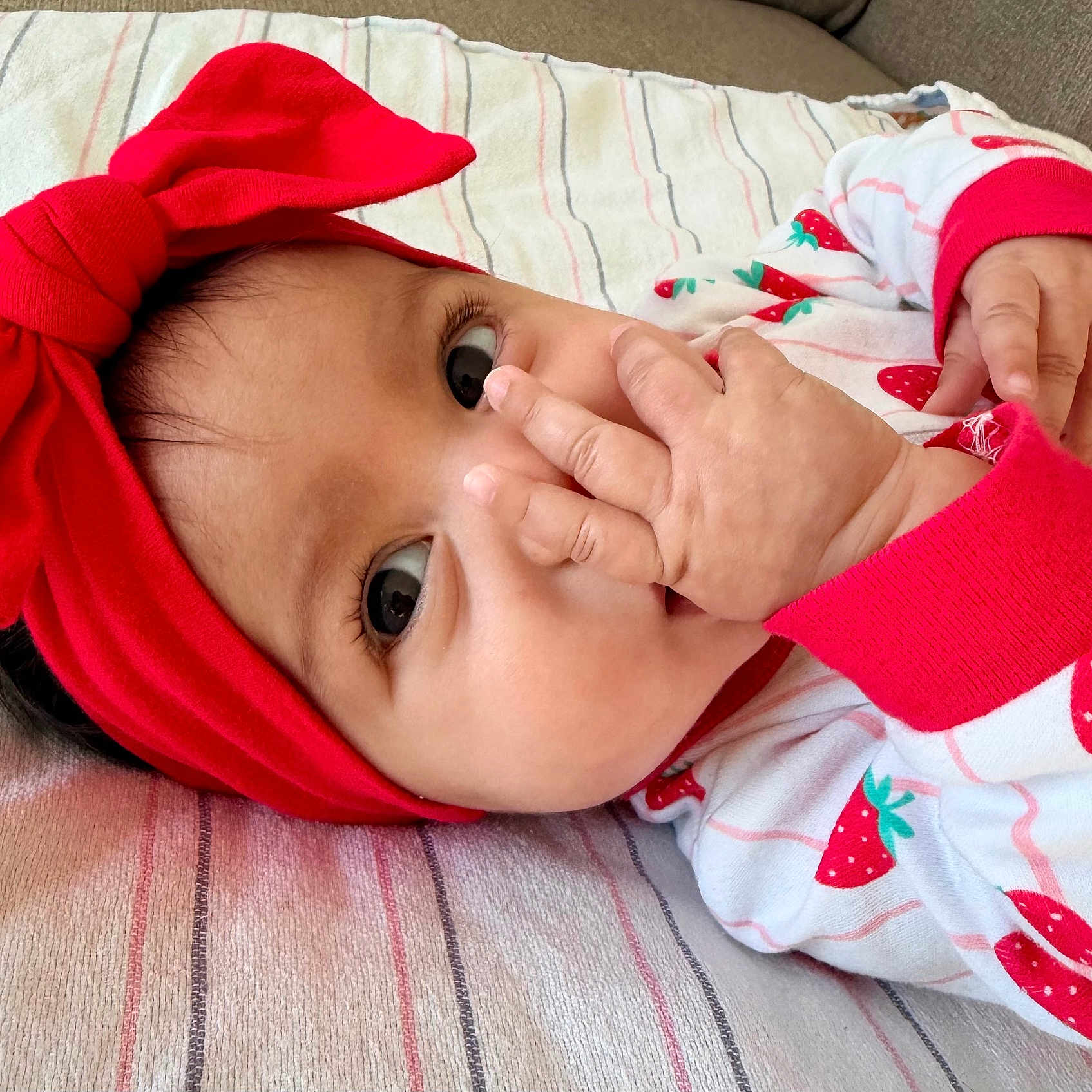 Maya Kamila joined the competition — help win amazing prizes! baby, baby_girl, blanket, child, clothing, cute, eyes, face, fingers, hand, headband, indoors, infant, lying_down, portrait, red_bow, skin, sleepwear, strawberry_pattern, striped