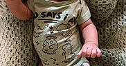 Elias joined the competition — help win amazing prizes! baby, infant, smiling, tongue_out, onesie, dinosaur_print, knitted_blanket, cozy, cute, happy, chubby_arm, lying_down, indoors, child, person, skin, head, hand, foot, red_bracelet