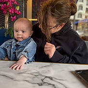Louka a rejoint le concours — aidez-le/la à gagner de superbes lots ! baby, child, woman, denim_jacket, black_hoodie, glasses, table, marble, flower, plant, indoor, portrait, person, urban, window, hand, face, casual_clothing, curious, seated