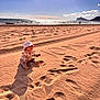 baby, beach, sand, ocean, footprints, hat, sun_hat, child, sky, clouds, water, mountain, shore, sunlight, nature, outdoor, seascape, person, sitting, summer