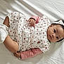 baby, infant, child, dress, headband, socks, white_blanket, lying_down, cute, portrait, indoors, soft_lighting, floral_pattern, pink_sleeves, hands, legs, dark_hair, expression, person, young