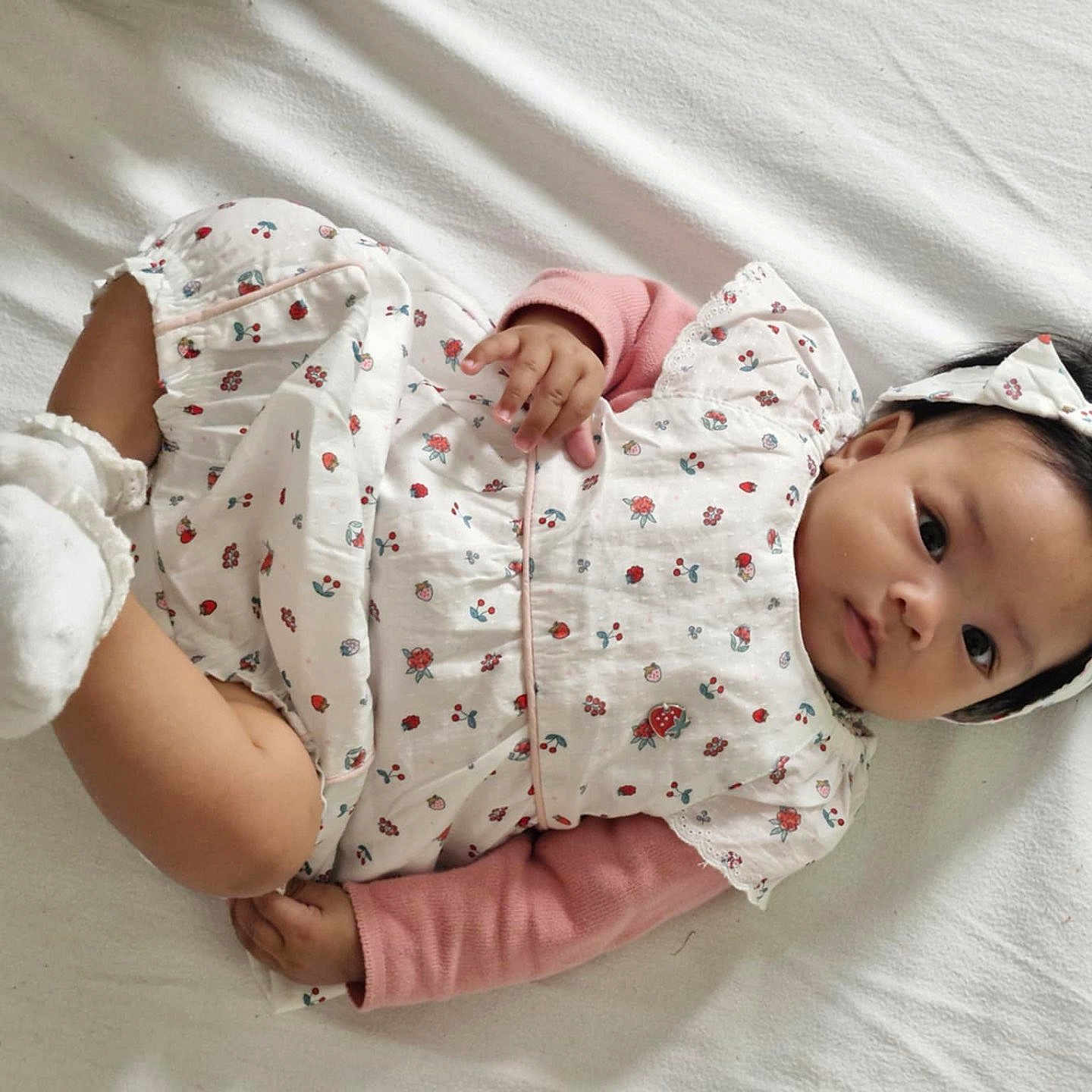 Myah participe au concours pour gagner de l'argent avec cette photo : baby, child, cute, dark_hair, dress, expression, floral_pattern, hands, headband, indoors, infant, legs, lying_down, person, pink_sleeves, portrait, socks, soft_lighting, white_blanket, young